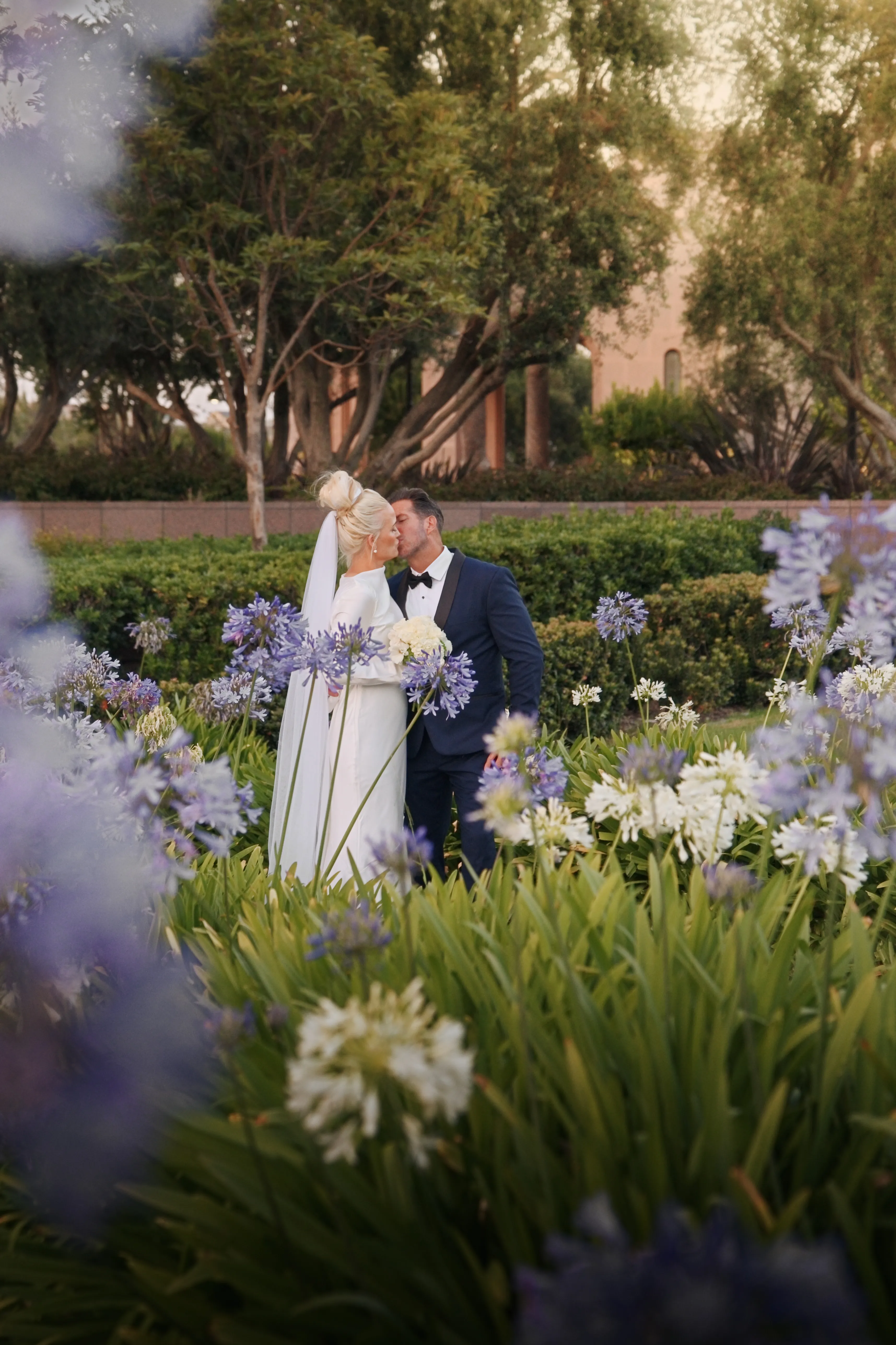 Bride and groom kiss framed by flowers at the Newport Beach Temple gardens