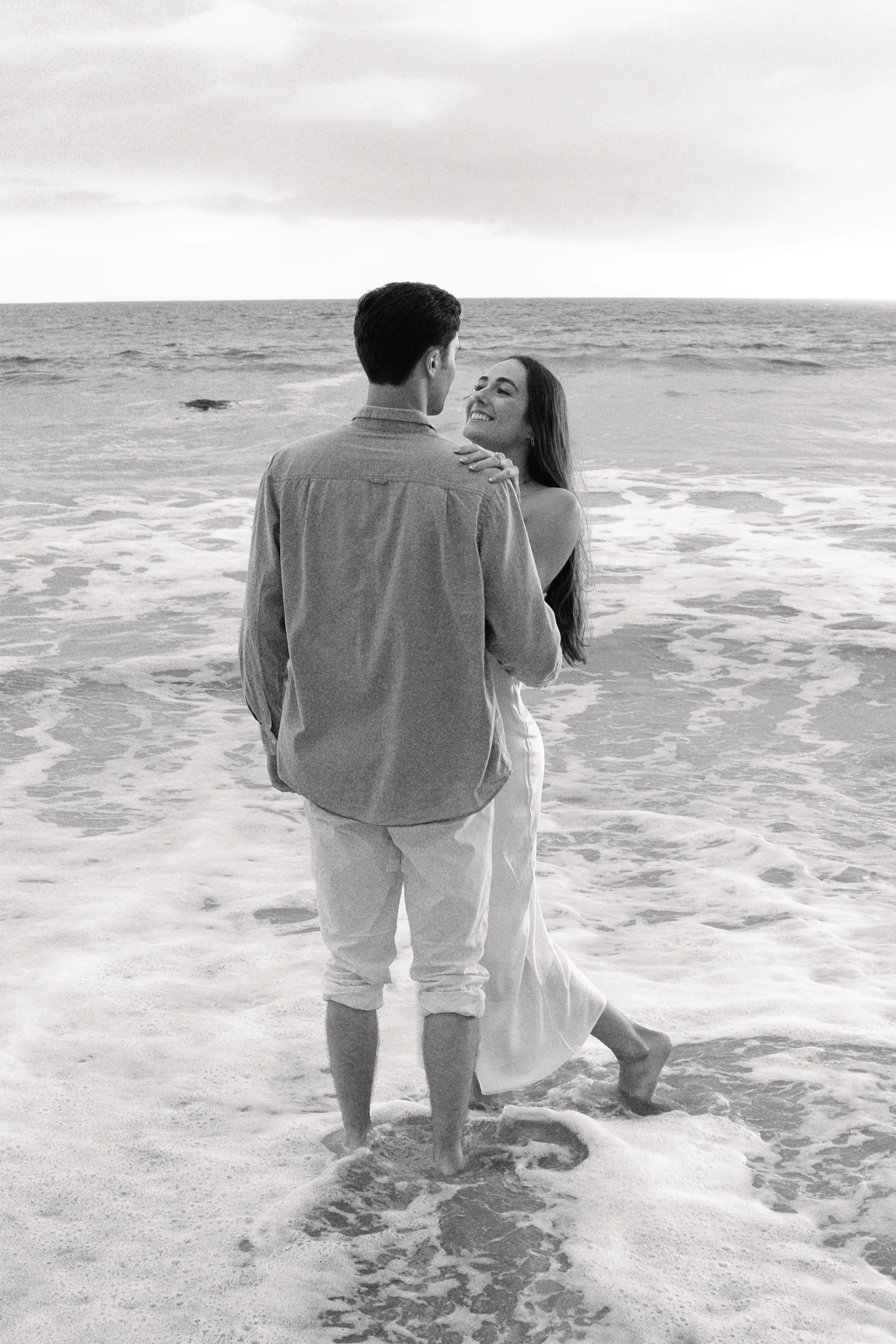 Black and white photograph of Roman and Grace by the surf at golden hour